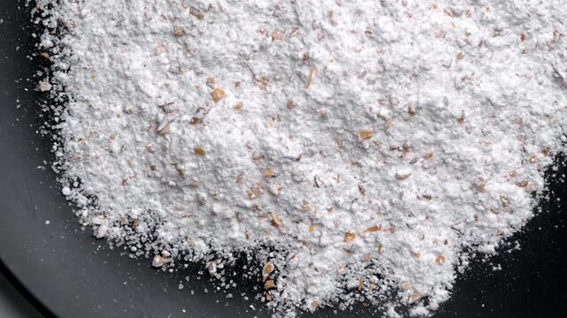 Fine sugar mixed with grated lemon zest on dark background. Baking ingredient texture. Top view