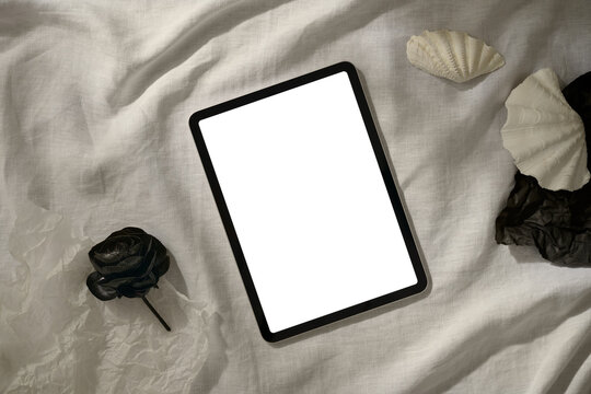 A modern tablet with a blank white screen is styled with seashells