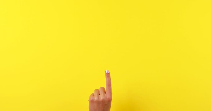 Close-up of a finger pointing upward on a bright yellow background. Gesture symbolizing attention, idea, instruction, warning, or important message. Minimal, isolated concept with copy space. 4K video