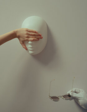 Hand covering face sculpture with glasses in hand