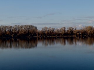 Wide Calm River with Smooth Water and Bare Trees Reflected at Dusk