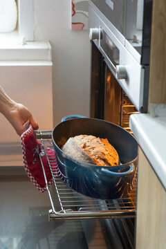 Hand pulling homemade sourdough bread from oven