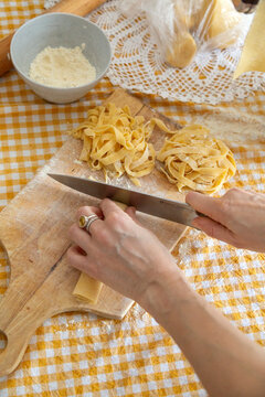 Hands cutting fresh pasta dough on wooden board