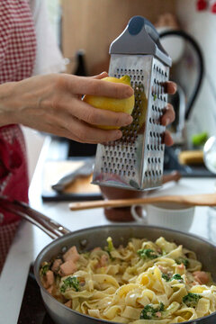 Person grating fresh lemon zest over pasta
