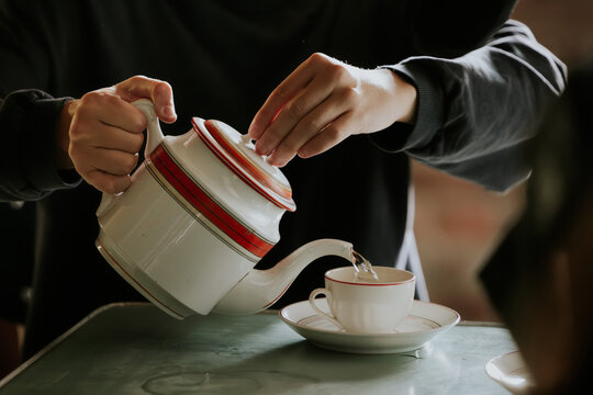 Pouring tea into elegant ceramic cup with saucer