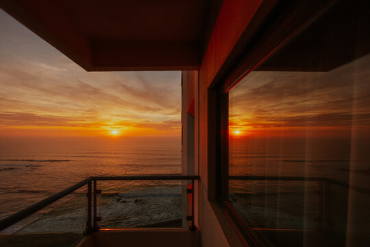 Ocean sunset view from a balcony with window reflection