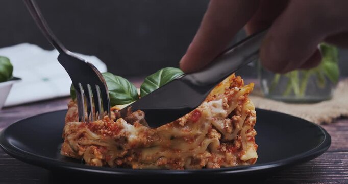 Close-up of hands using knife and fork to cut into a portion of lasagna, highlighting Italian cuisine, gastronomy, and gourmet dining.