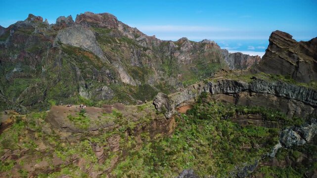 Aerial sideways tracking shot of PR1 Vereda do Areeiro trail, drone flying low revealing Stairway to Heaven and hikers on narrow volcanic ridges under bright sun, epic colorful mountains in Madeira.