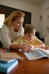 Mother checking her son&rsquo;s homework and studying lessons together at home. Warm family scene showing care, support and learning in everyday domestic life.