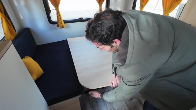 High-angle view of a man transforming the dining area of a small camper into a comfortable sleeping space, showcasing convertible furniture