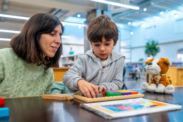 Teacher helping young boy playing learning game puzzle