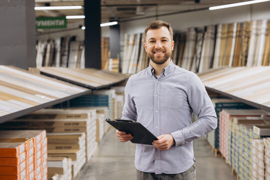 Smiling man holding a clipboard, standing in a hardware store showing flooring samples, sales consultant