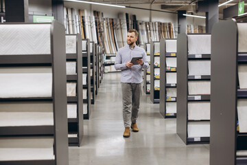 Sales assistant holding digital tablet navigating through floor tile samples in a modern home improvement store