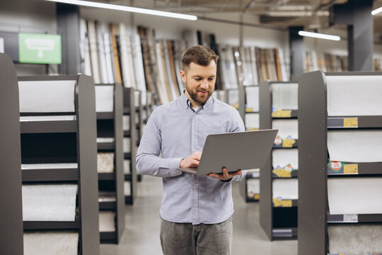 Man smiling while checking inventory and managing stock in a large retail business interior using a laptop