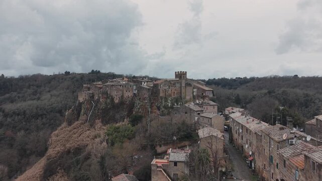 Aerial view of Calcata Vecchia, an ancient medieval village perched on a rocky cliff in Lazio, during a gloomy day. Historic stone houses surrounded by forest and dramatic landscape of a scenic view.
