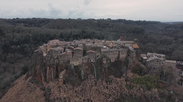 Aerial view of Calcata Vecchia, an ancient medieval village perched on a rocky cliff in Lazio, during a gloomy day. Historic stone houses surrounded by forest and dramatic landscape of a scenic view.
