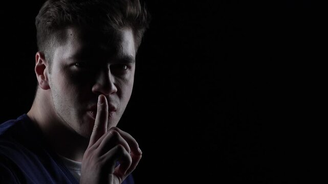 4K cinematic dark portrait of angry young man turning from profile to camera making silence gesture in dramatic lighting