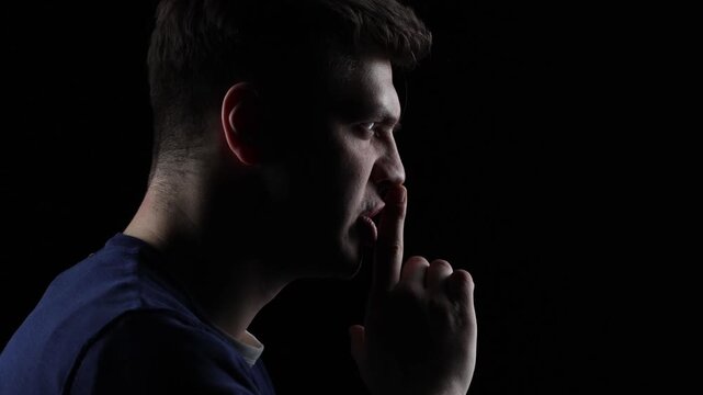 4K cinematic side portrait of angry young man making silence gesture in dramatic dark lighting