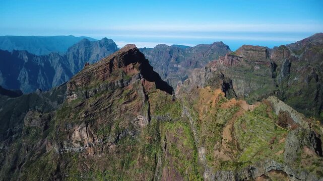Aerial diagonal flyover of PR1 trail in Madeira, drone approaching narrow mountain ridge with hikers at Pedra Rija and Stairway to Heaven, sunlit volcanic cliffs and distant horizon, cinematic.