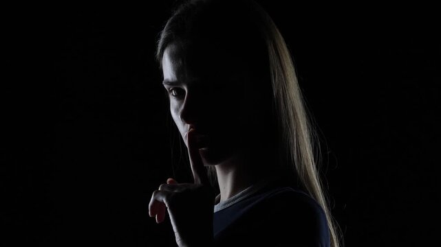4K cinematic dark portrait of serious young woman turning to camera making silence gesture in dramatic lighting