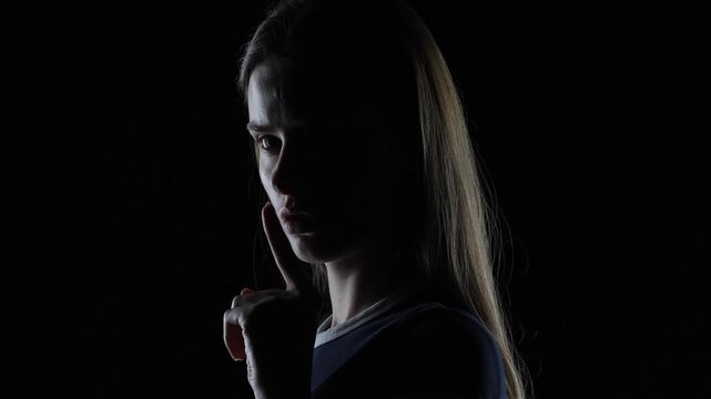 4K cinematic dark portrait of serious young woman making silence gesture and shaking head in dramatic lighting