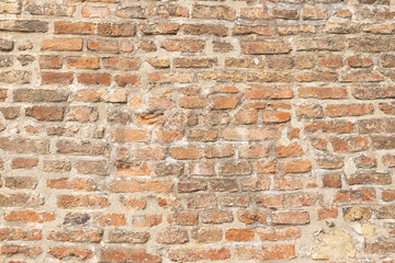 Fototapeta premium Textured brick wall with a mix of red and brown bricks, showcasing weathered mortar and uneven surfaces, ideal for backgrounds or architectural designs