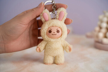 Fototapeta premium Hand holding a cute plush bunny costume keychain with a grumpy facial expression against a soft blurred background