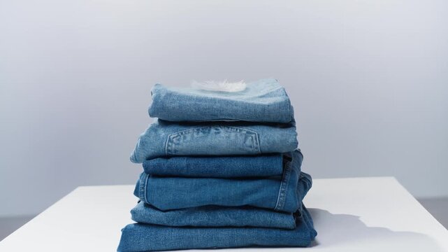 Stack of neatly folded blue denim jeans with a soft white feather on top.