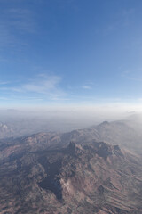 Aerial View Of Vast Mountain Desert Landscape Under Clear Blue Sky And Distant Peaks At Dawn