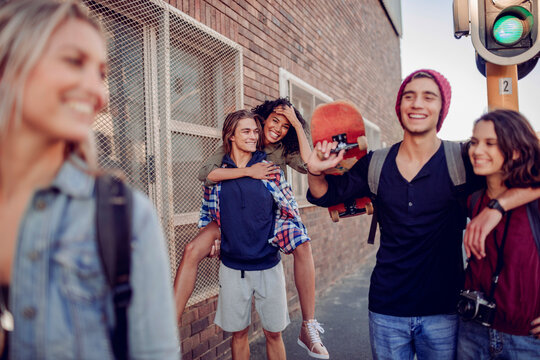 Happy teenage friends walking on city street with skateboard