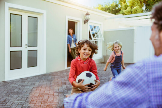Happy children playing soccer in backyard with parents