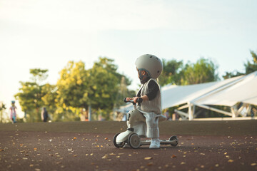 Cute toddler child wearing a safety helmet sitting on a balance bike scooter in a sunny outdoor park. Childhood active play safety awareness and physical development concept.