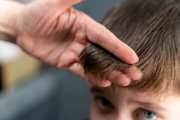 Fototapeta premium Child with light brown hair having bangs styled by an adult hand, close-up view focusing on hair texture and grooming in a domestic setting