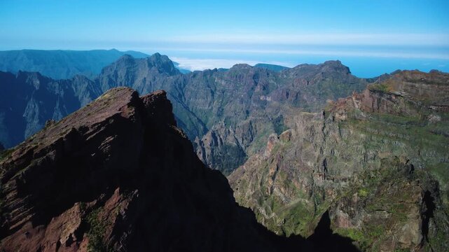 Aerial flyover of rugged volcanic peaks at Pico do Areeiro, drone flying over sunlit and shadowed cliffs into the wild mountain wilderness, cinematic landscape above the clouds in Madeira, epic.
