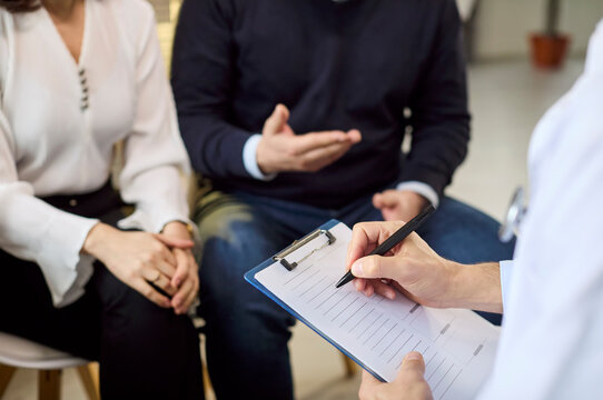 Doctor couple consultation with clipboard and notes. Focus on fertility and pregnancy planning with the physician writing details in a calm clinic. Simple family planning concept for care.