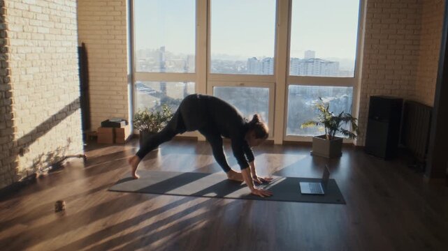 Calm man holds down dog stretch yoga pose near tall window studio