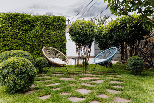 Cozy garden seating area with two outdoor lounge chairs, table, lawn and trimmed shrubs