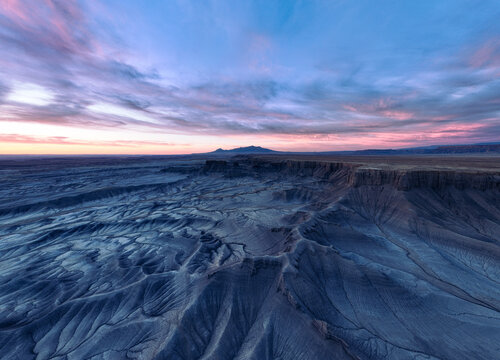 Aerial view of a surreal landscape where the rugged, textured earth meets the soft pastel hues of the dawn sky, Hanksville, Utah, United States.
