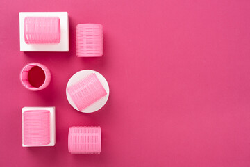 Obraz premium Pink hair curlers on color background, top view