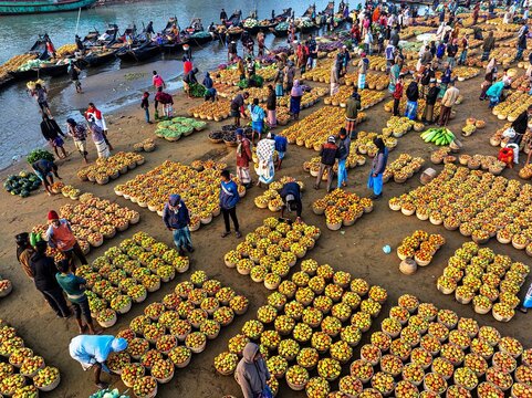 Kanaighat, Bangladesh - 07 February 2026: Aerial view of vibrant marketplaces bustling with activity, showcasing an array of colorful fruits and vegetables near the river.