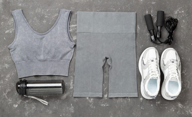 Woman sportwear outfit with equipment on concrete background, top view