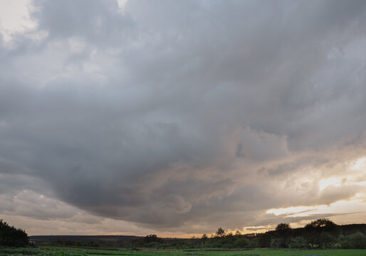 Dramatic thunderous sunset sky with dark huge rain clouds over green forest