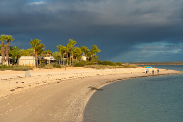 Obraz premium Romantic Monkey Mia beach at sunset with calm ocean waves and silhouetted coastal dunes backdrop
