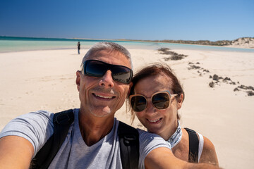 Obraz premium Smiling tourists couple posing together on idyllic Coral Bay beach with clear ocean waves and tropical palms WA holiday destination