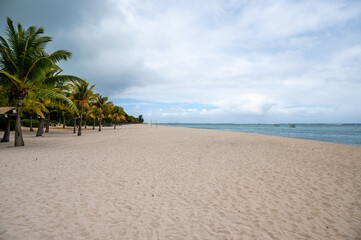 Wide view of an empty white sand beach with palm trees and turquoise ocean in Le Morne, Mauritius