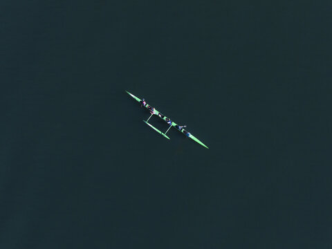 Aerial view of a vibrant green outrigger canoe cutting through the deep blue waters near Caporn Street, Mosman Park, Western Australia, Australia.