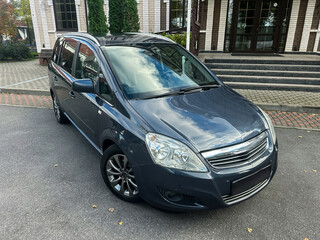 Dark gray car parked in front of a modern building surrounded by greenery on a clear day