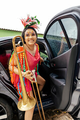 Young woman in colorful carnival costume stepping out of a car holding a trombone, arriving excited...