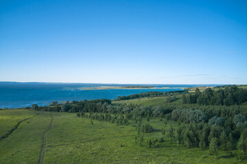 A picturesque panoramic view of the left bank of the Kama River. The riverbed, floodplain meadows, and a slope with green groves and meadows. Summer. Drone footage.