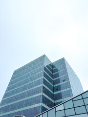 Obraz premium Tall glass building reaches into the sky with reflective surfaces and bright light at midday in a cityscape environment